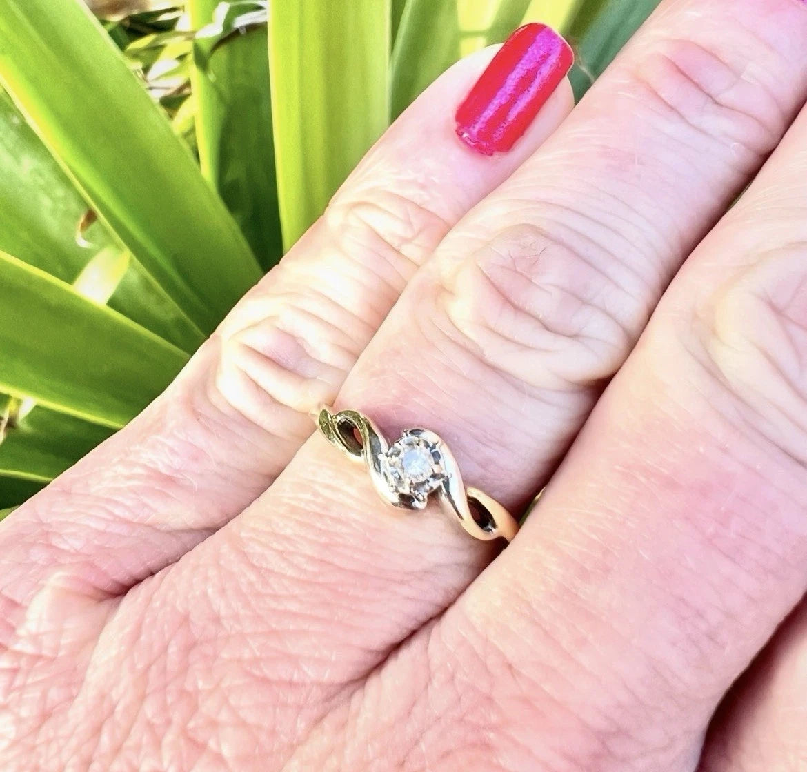 Gold ring with a diamond on a person's finger against a green leafy background