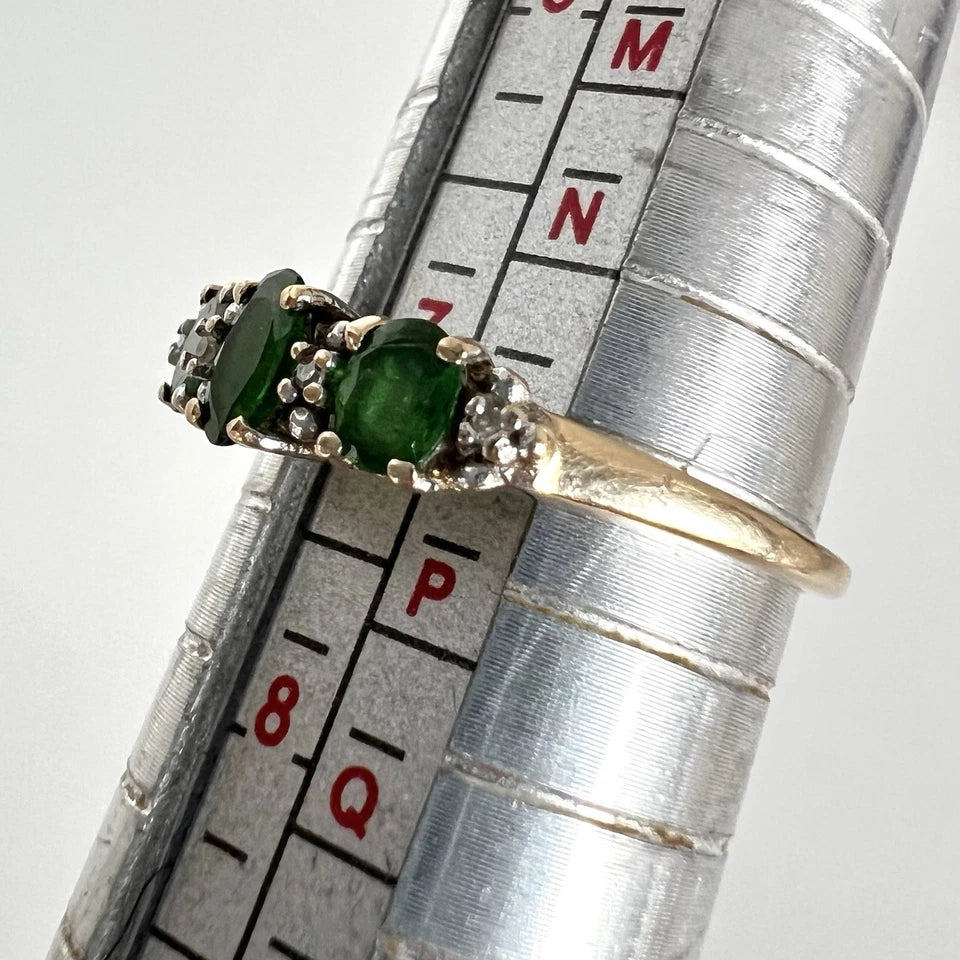 Gold ring with green gemstones on a ruler for size reference