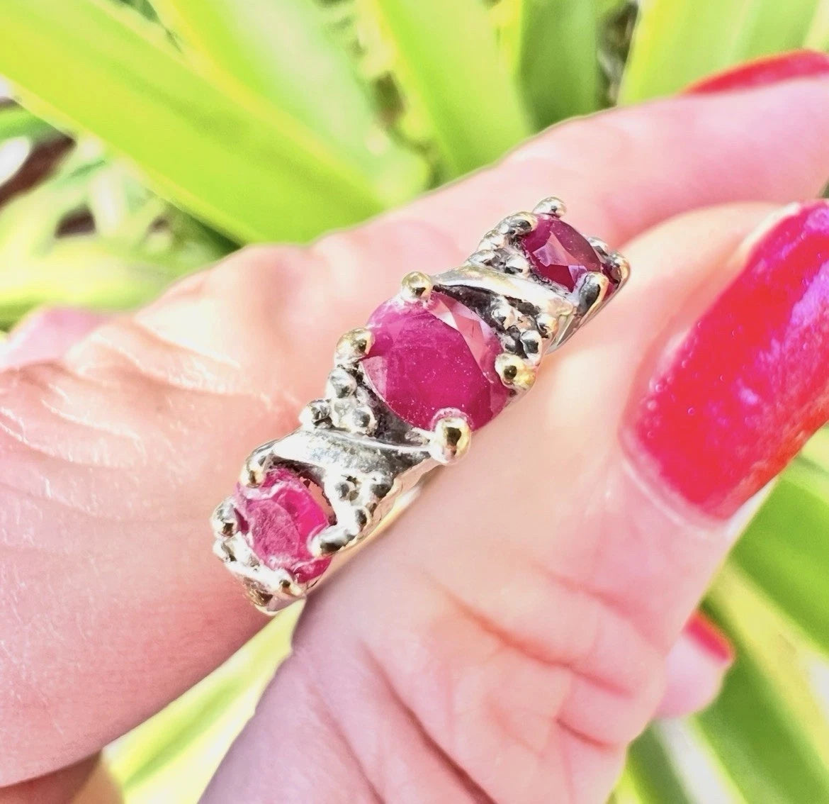 Gold ring with red ruby gemstones and diamonds on a hand against a green leafy background