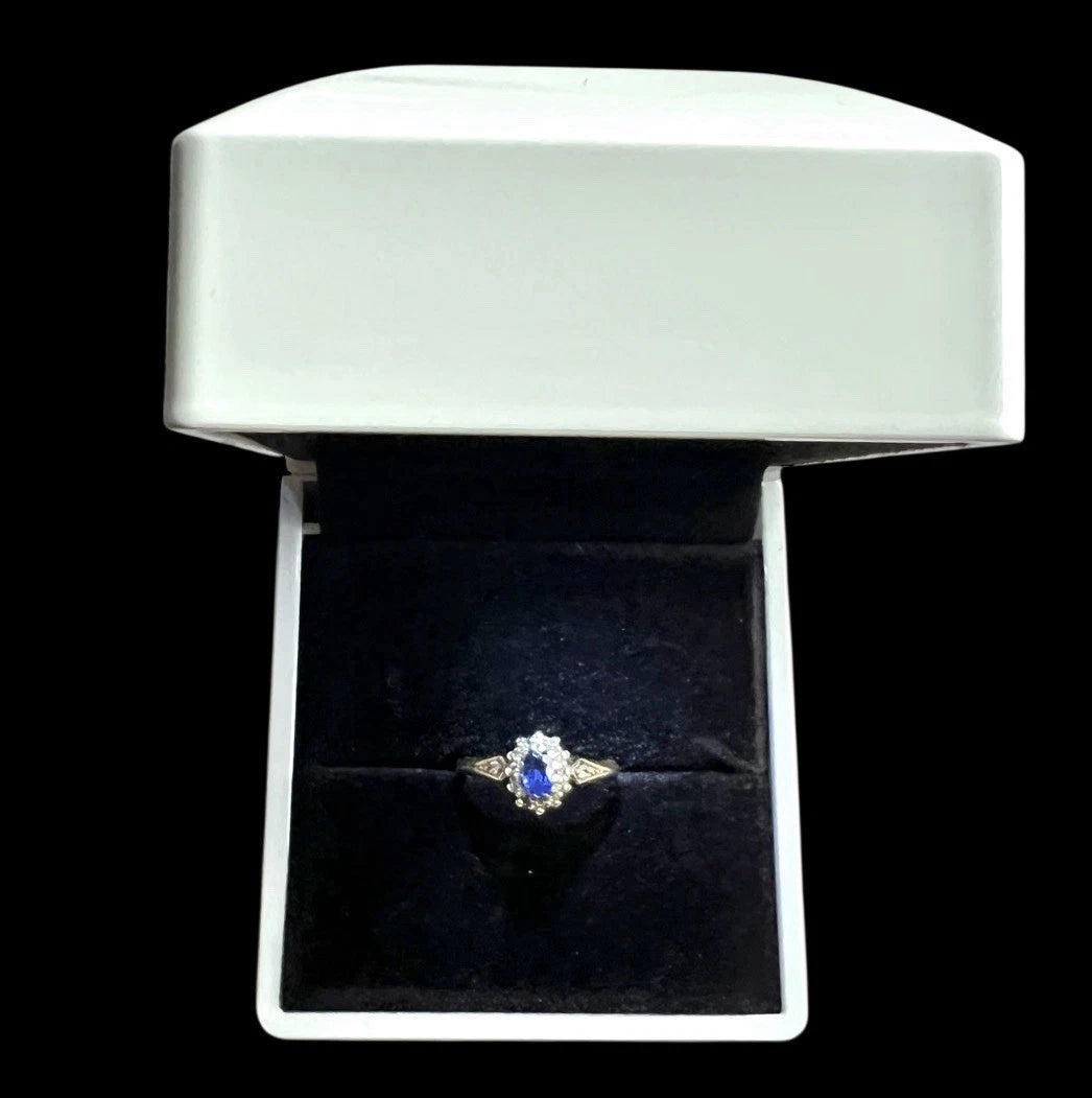 Diamond ring with blue sapphire gemstone and diamond halo in a white box on a black background