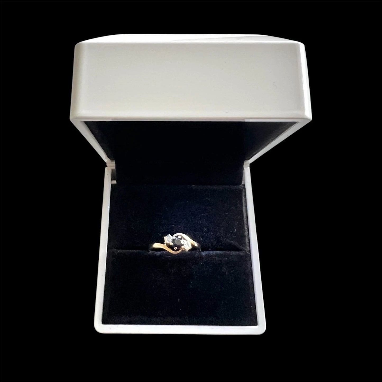 Gold ring with a sapphire and diamond in a white jewellery box on a white stand against a black background
