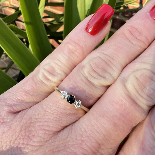 Hand wearing a ring with a sapphire and diamond accents against a green leafy background