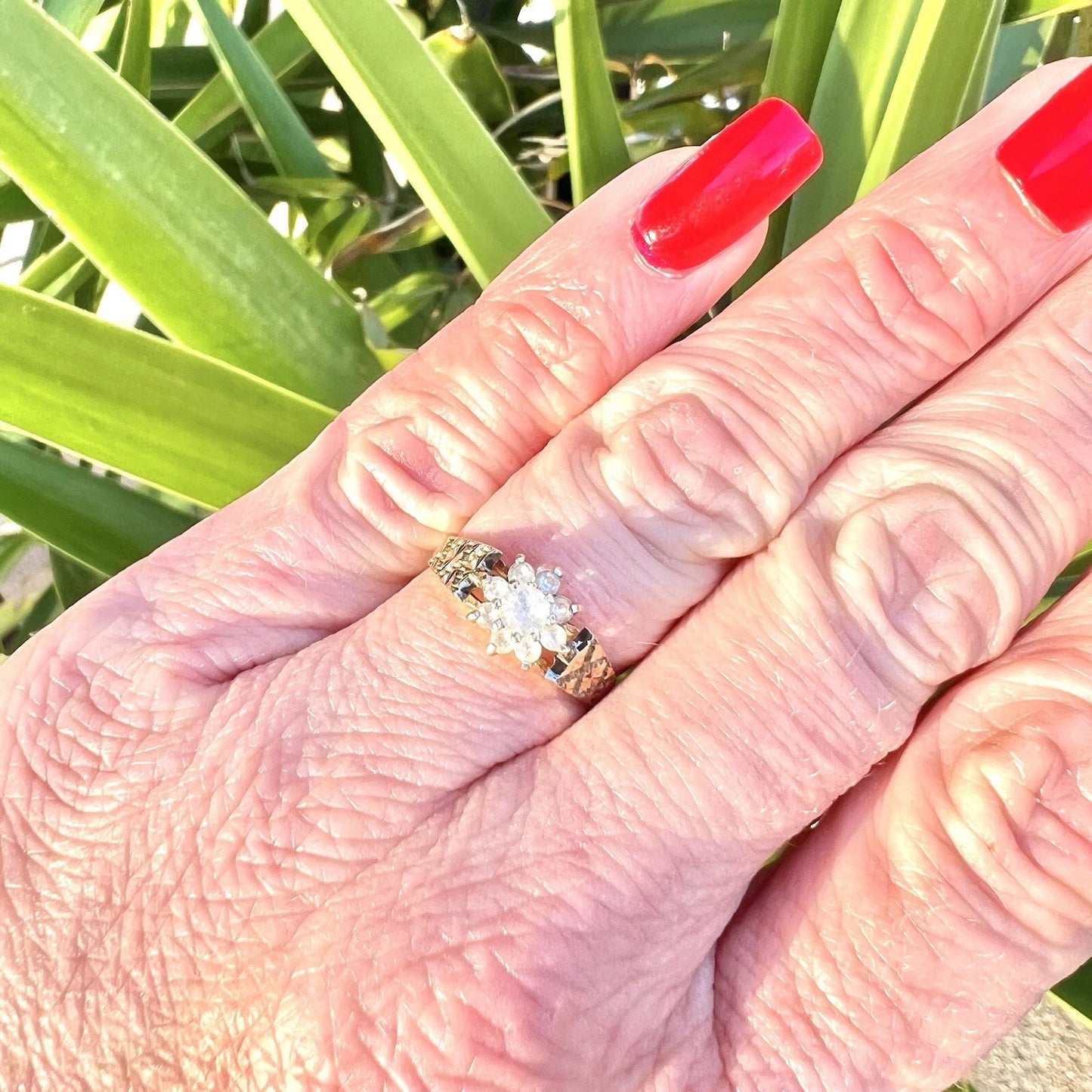 Hand wearing a ring with a blue topaz, set against a green leafy background