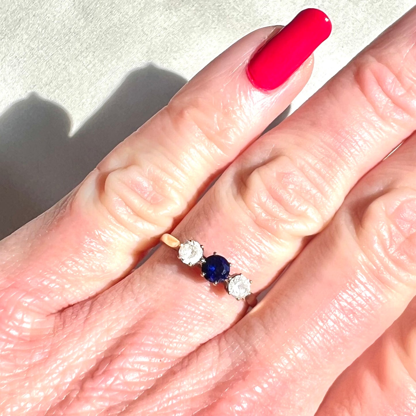 Close-up of a hand wearing a ring with a blue gemstone and two smaller stones.