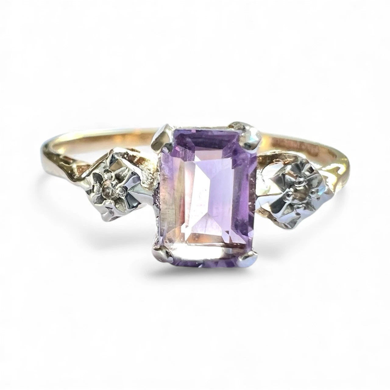 Close up view of gold ring with a purple amethyst gemstone and two smaller diamonds on a white background
