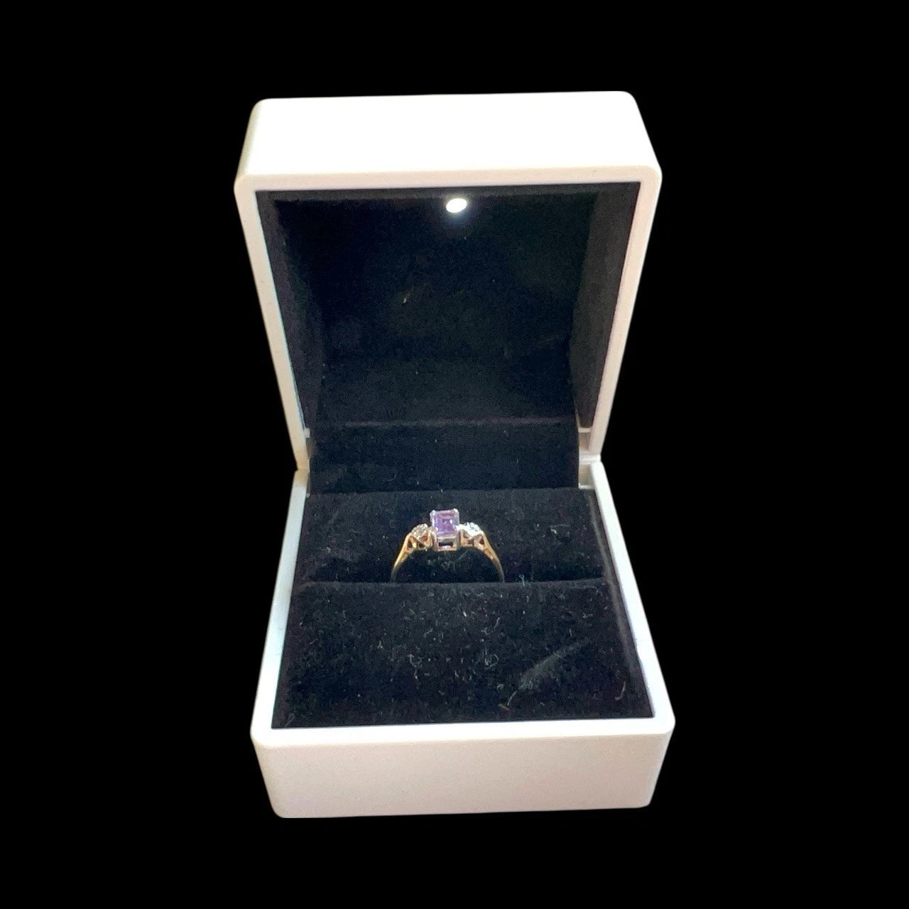 Gold ring with a purple amethyst gemstone and diamonds in an open jewellery box on a black background