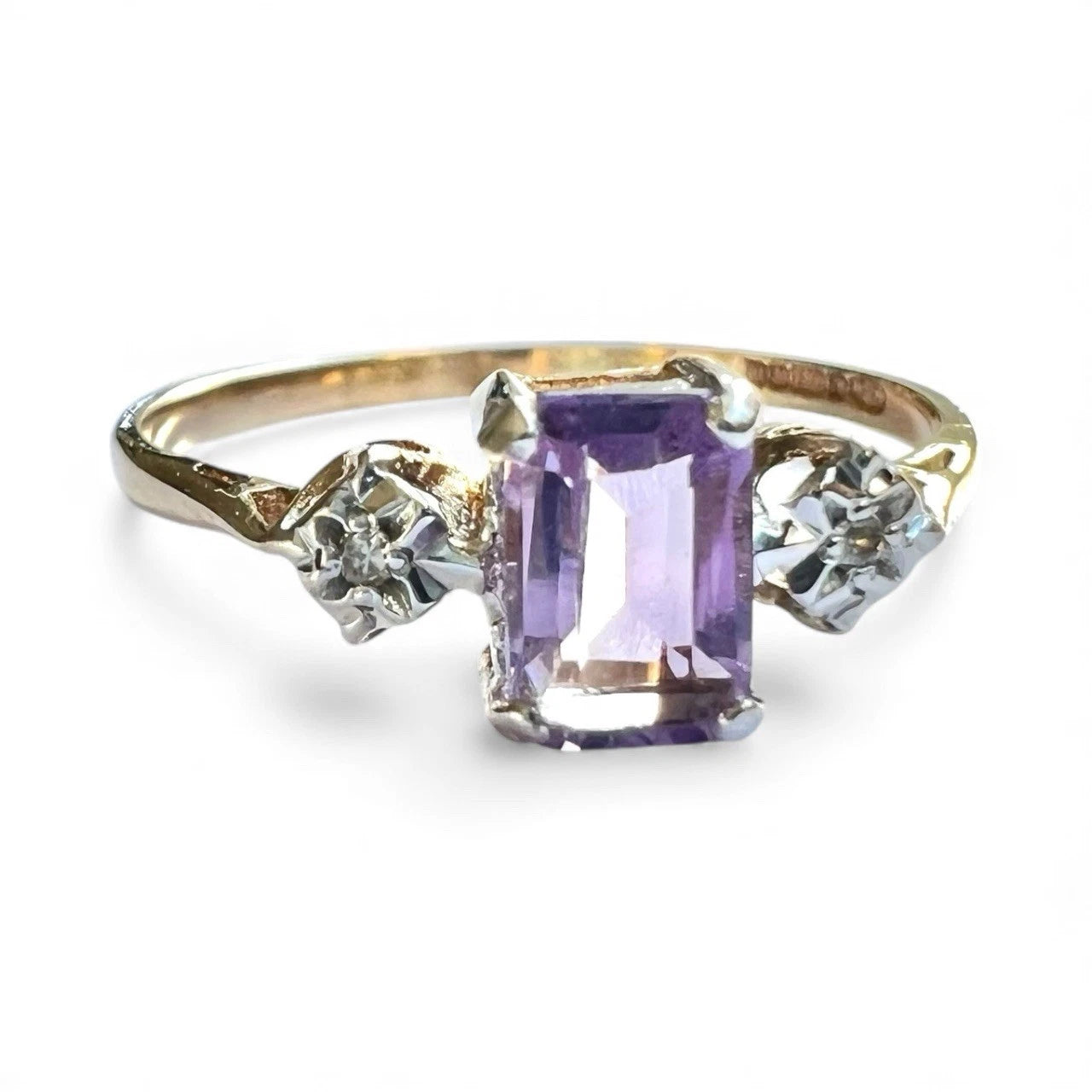 Three stone gold ring with a purple amethyst gemstone and diamond accents on a white background