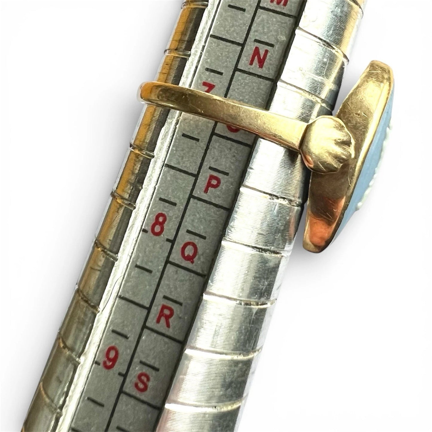 Close-up of a metallic ring sizer gauge with a gold ring on a white background