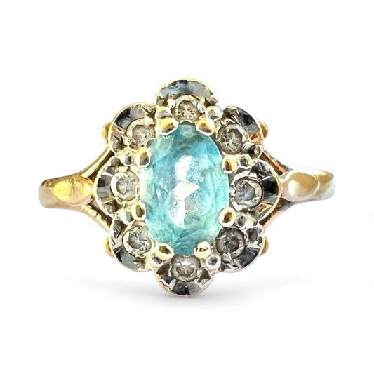 Gold ring with a central blue topaz gemstone and diamond halo on a white background