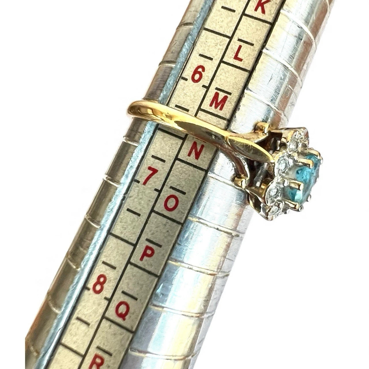 Gold ring with blue topaz gemstone and diamonds on a metal ruler for size measurement