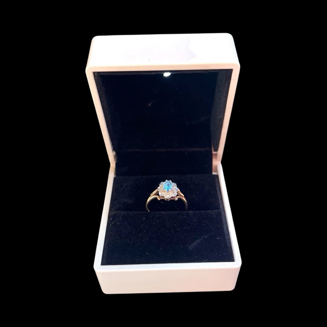 Gold ring with a blue topaz gemstone and diamond halo in a jewellery box on a black background
