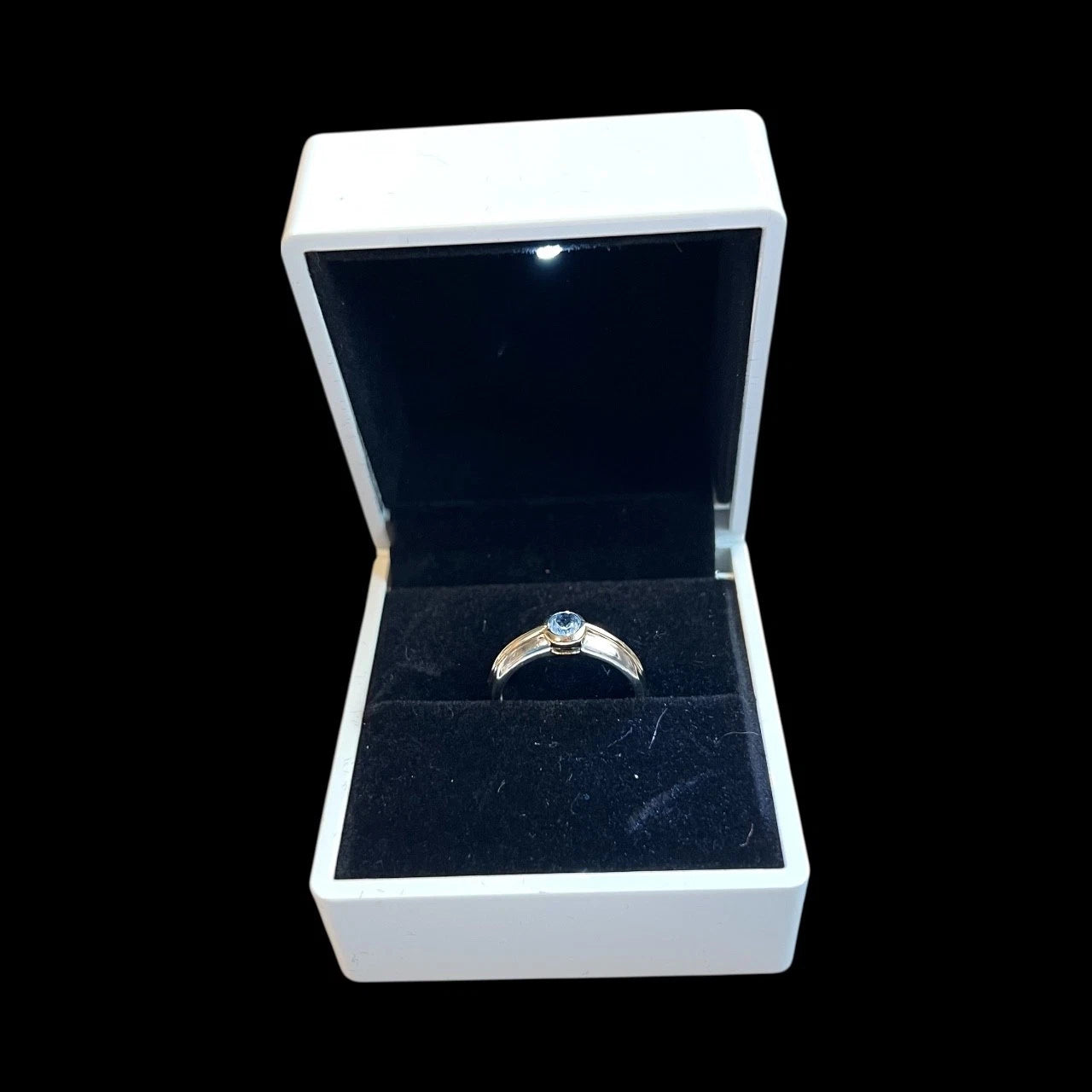 Gold ring with a blue topaz gemstone in an open jewellery box on a white background