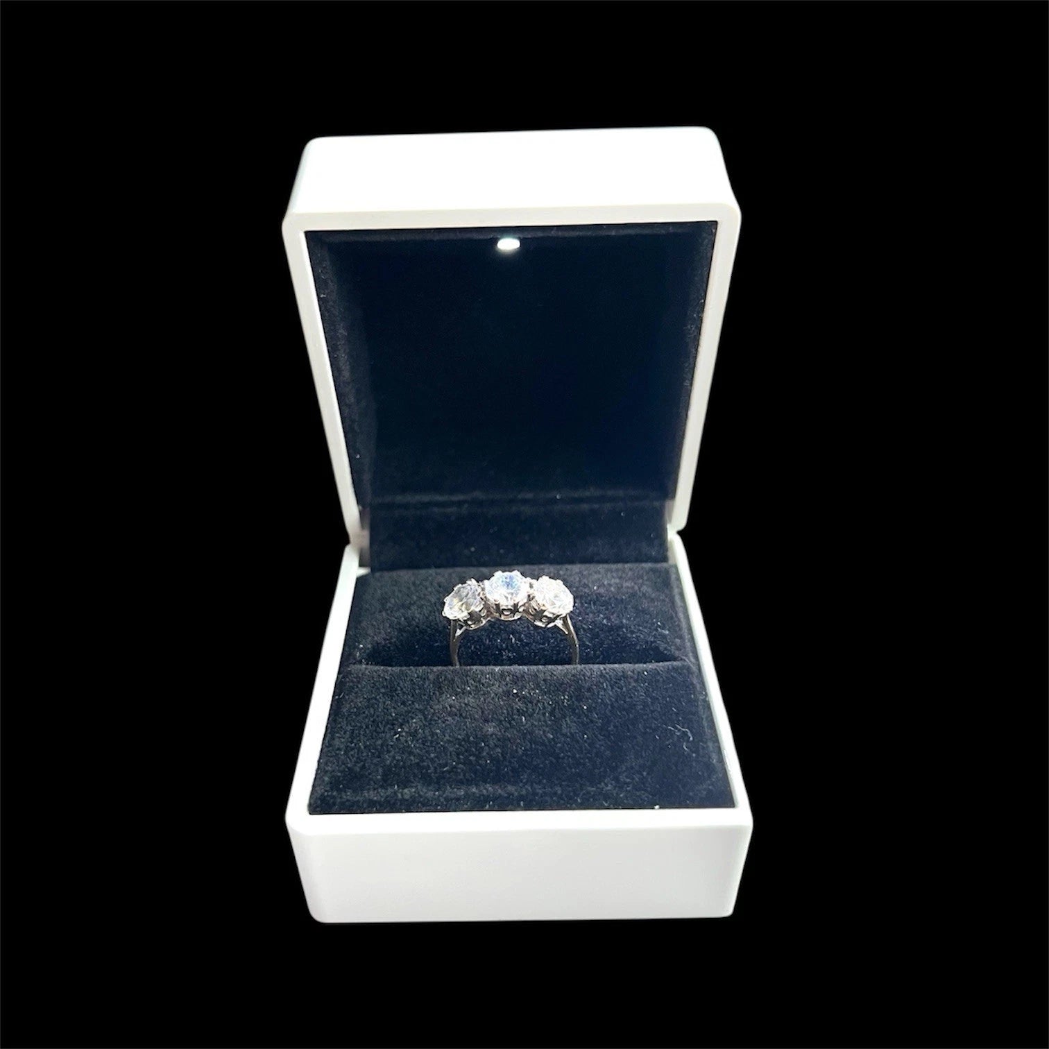 Three Stone Gold ring in a white jewellery box with a black background