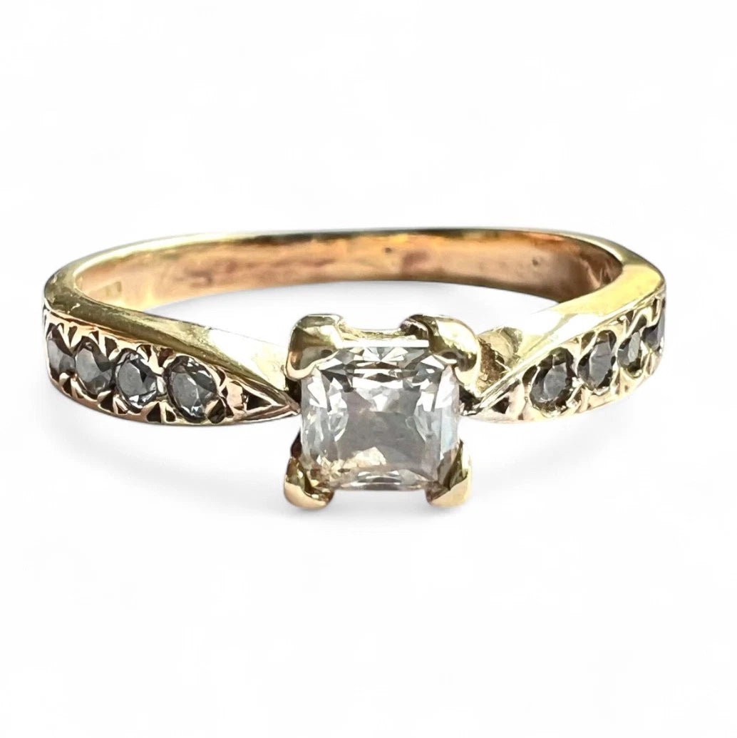 Gold ring with a central cubic zirconia and smaller CZ on the band against a white background, close up front view of setting 