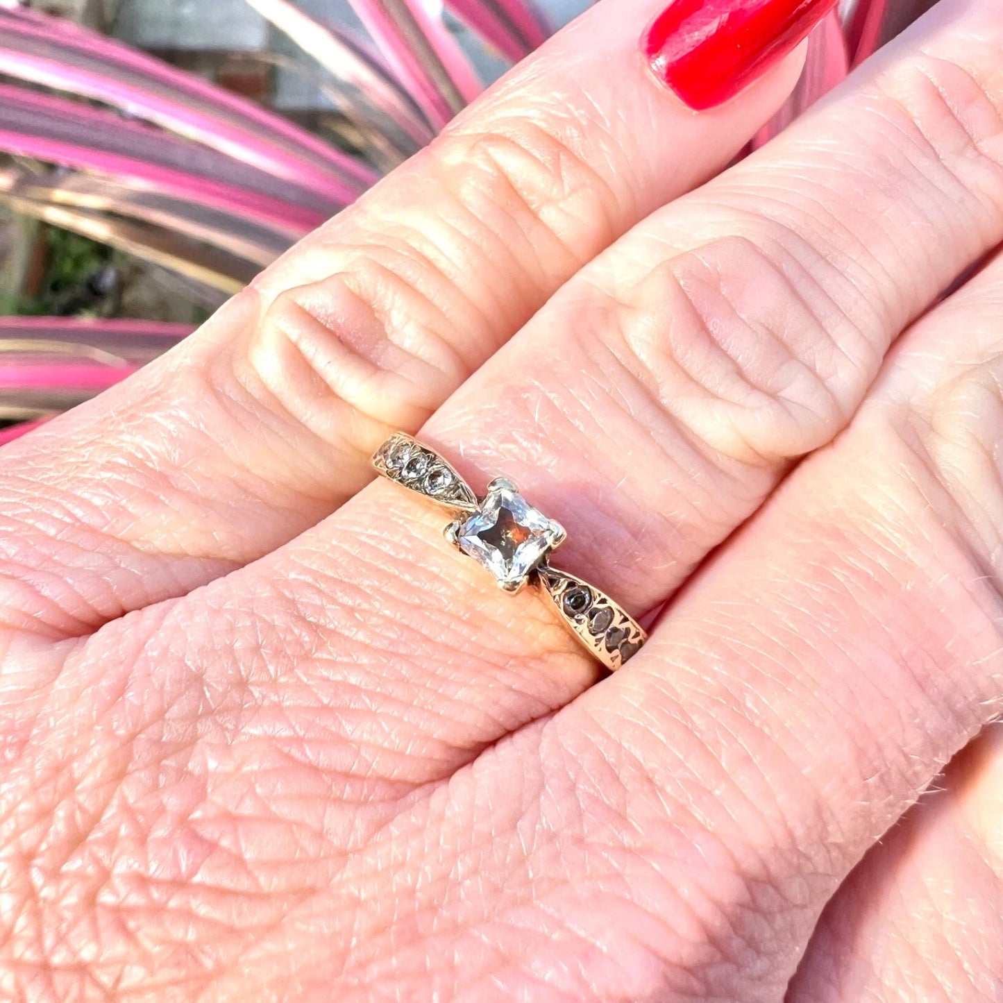 Close-up of a hand wearing a CZ solitaire  ring with assents on a pink background