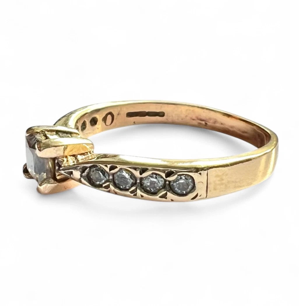 Gold ring with embedded CZ on a white background, close up side view of assents 