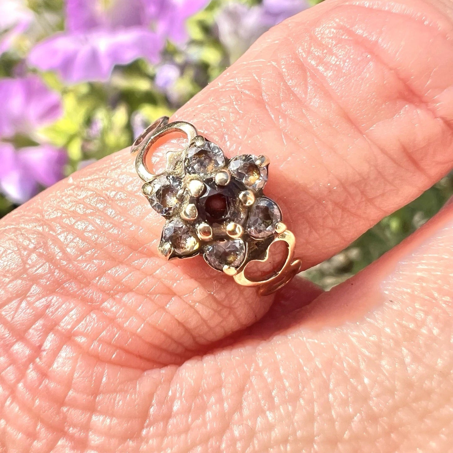 Gold floral ring on a finger with blurred purple flowers in the background
