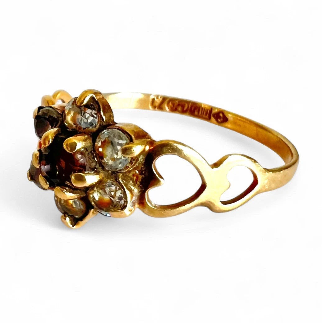 Gold ring with gemstones and heart detailed band on a white background