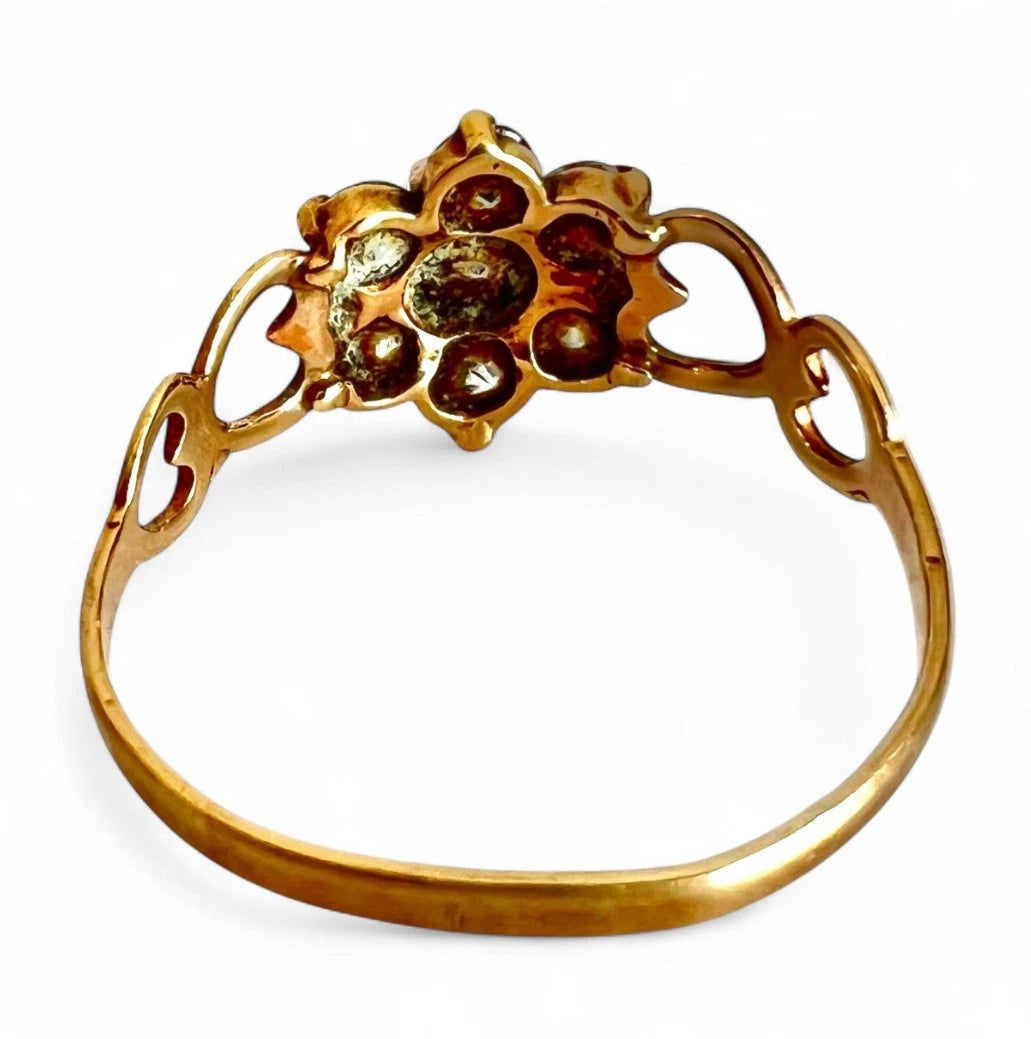 Gold ring with floral design and embedded stones on a white background, close up view of setting and gold band