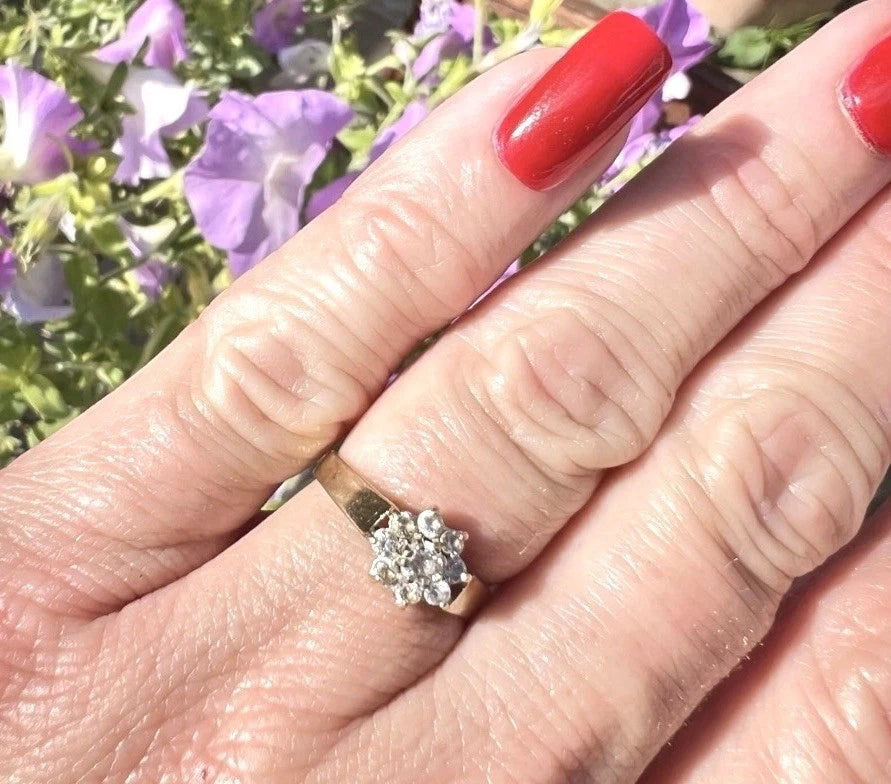 Hand wearing a cubic zirconia flower cluster ring with a blurred floral background