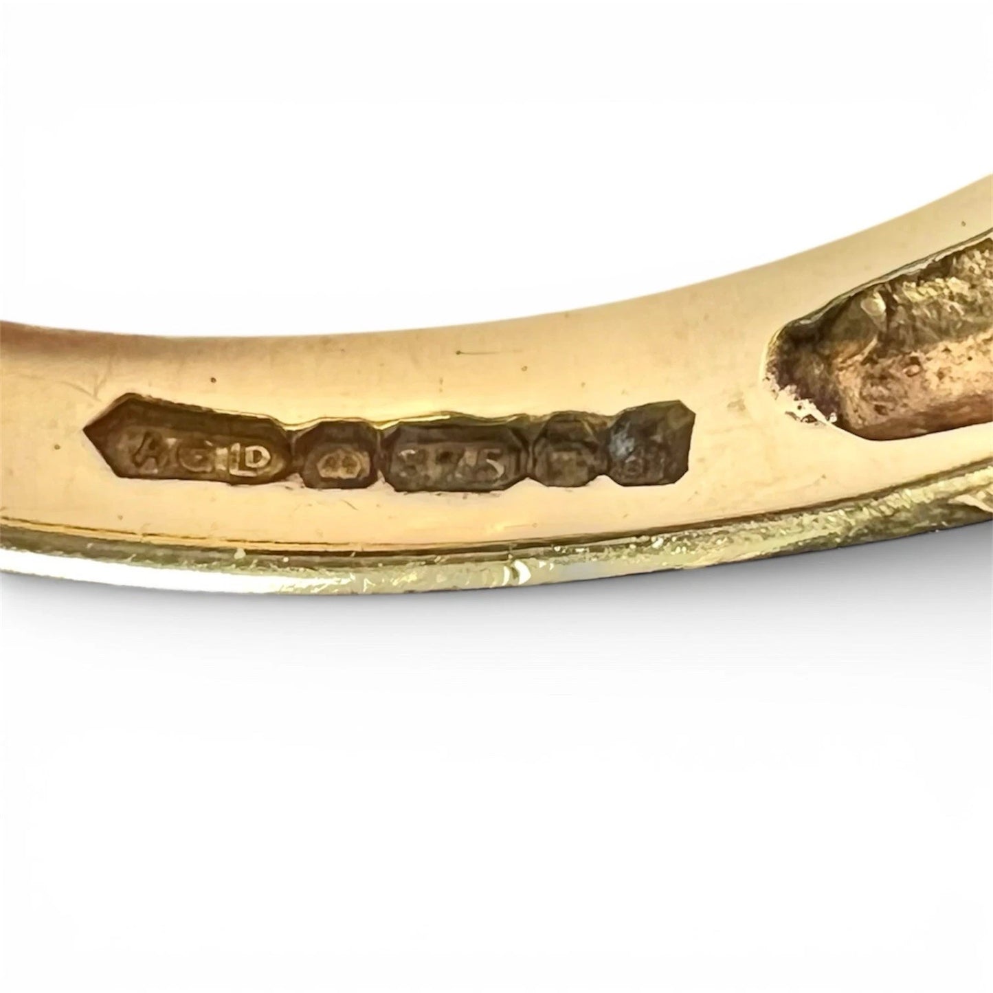 Close-up of a gold ring with engraved hallmark on a white background