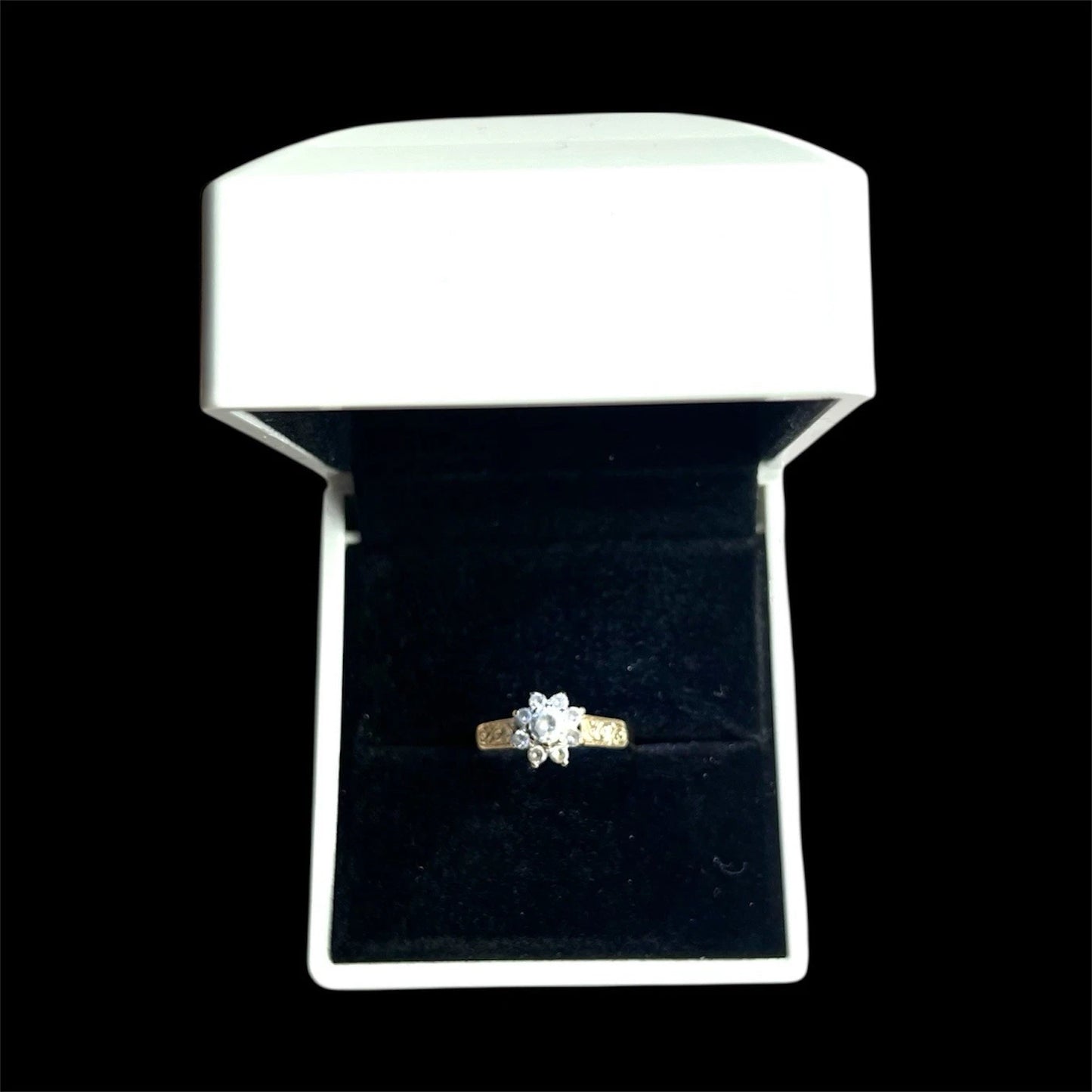 Gold ring with a cubic zirconia on a black velvet cushion in a white jewellery box.