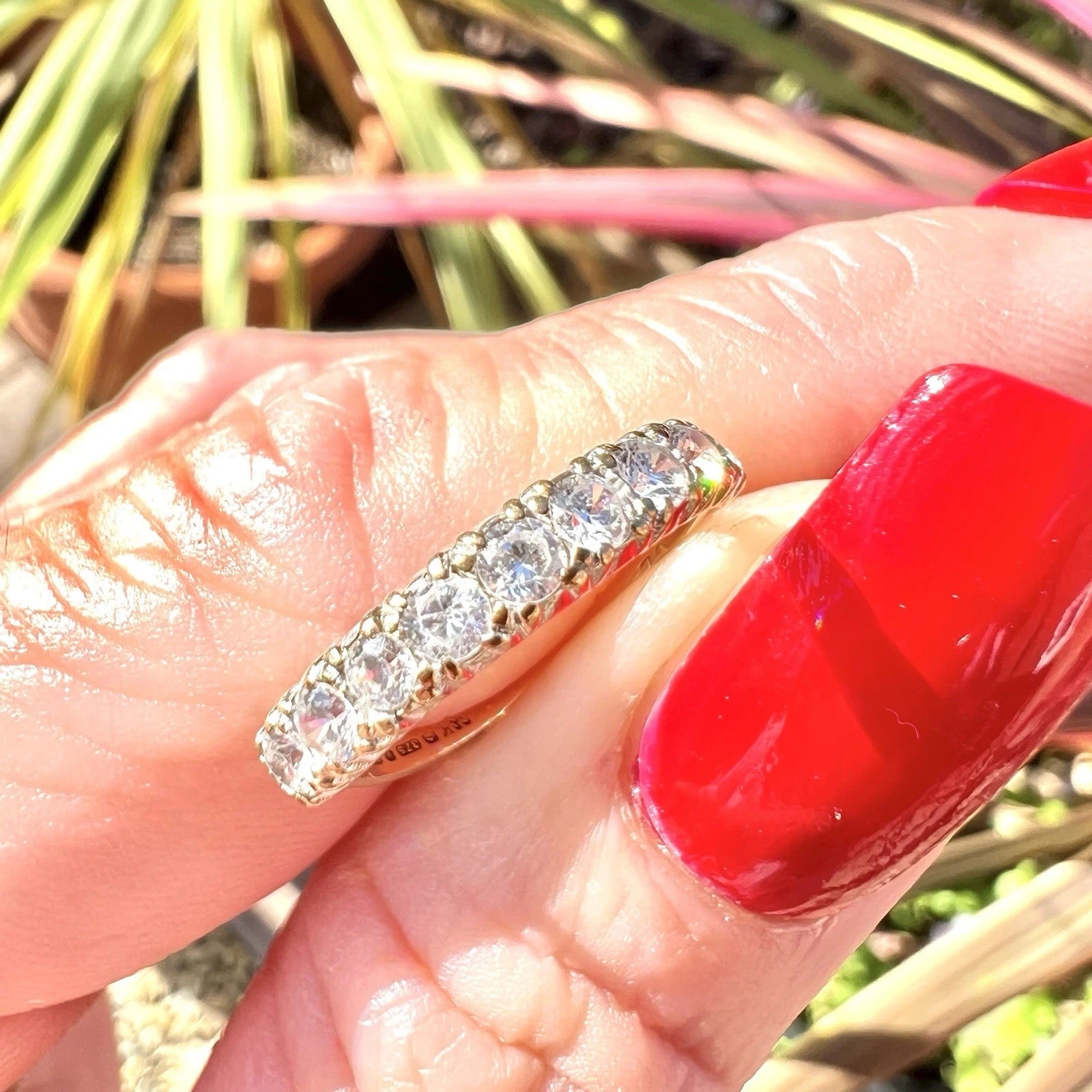 Cubic Zirconia ring on a hand with red nail polish against a blurred natural background