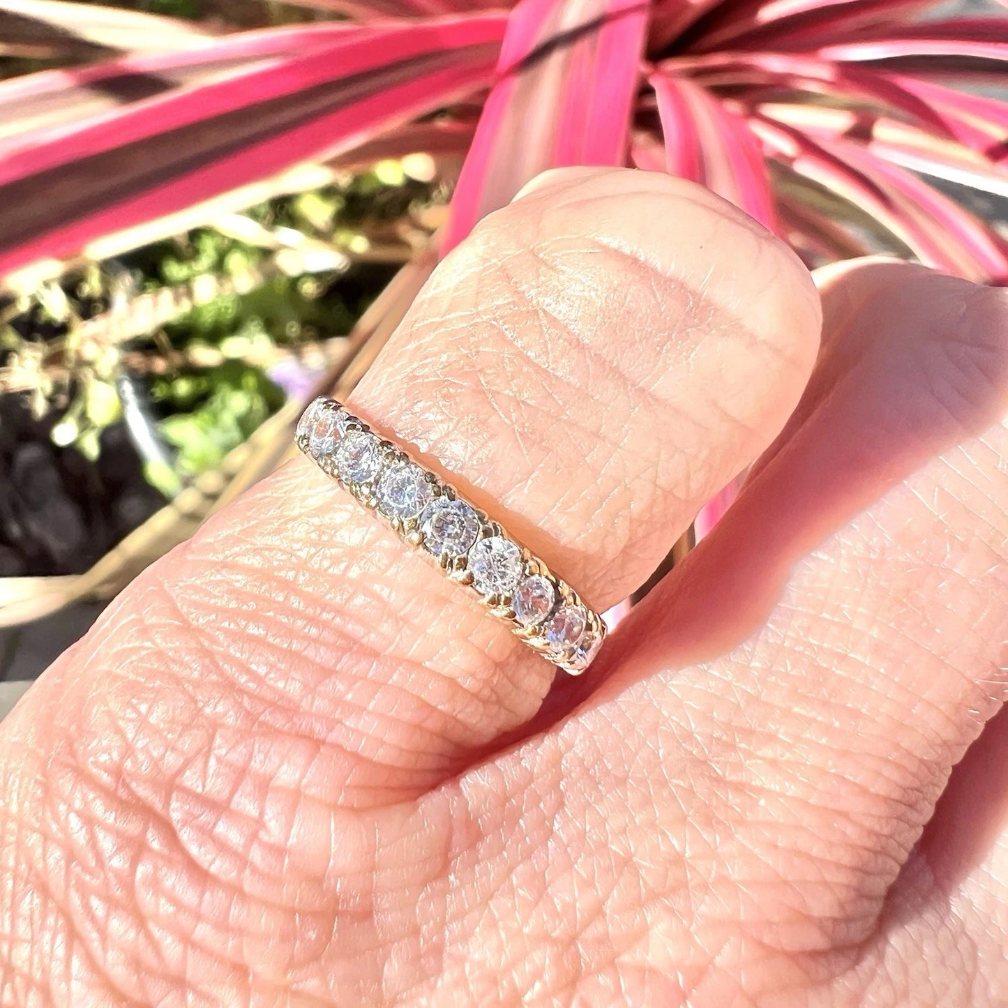 Gold ring with Cubic Zirconia on a finger against a blurred plant background