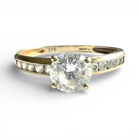 Gold ring with a large CZ and smaller CZ on the band against a white background