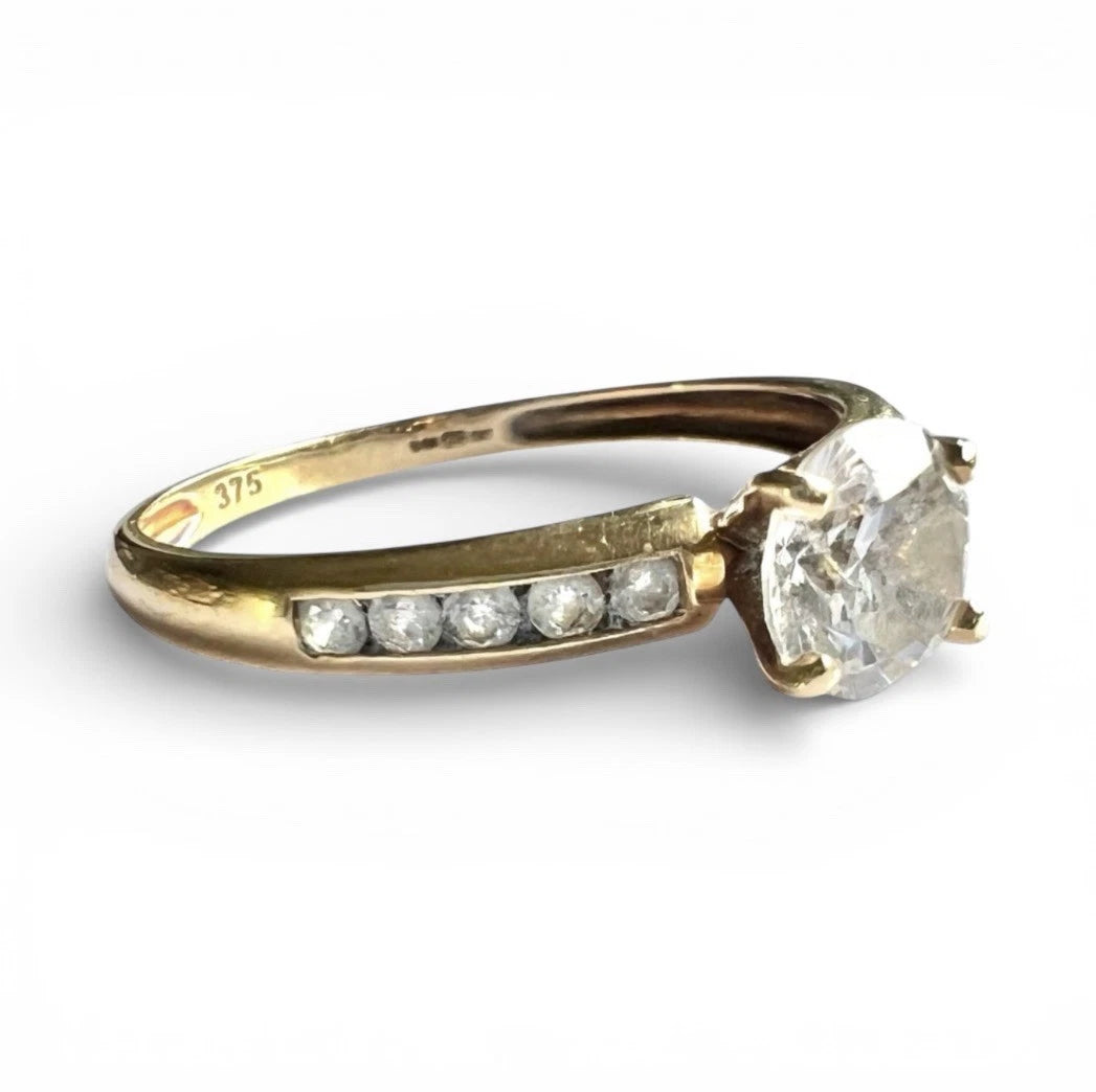 Gold ring with a large CZ and smaller CZ on the band against a white background