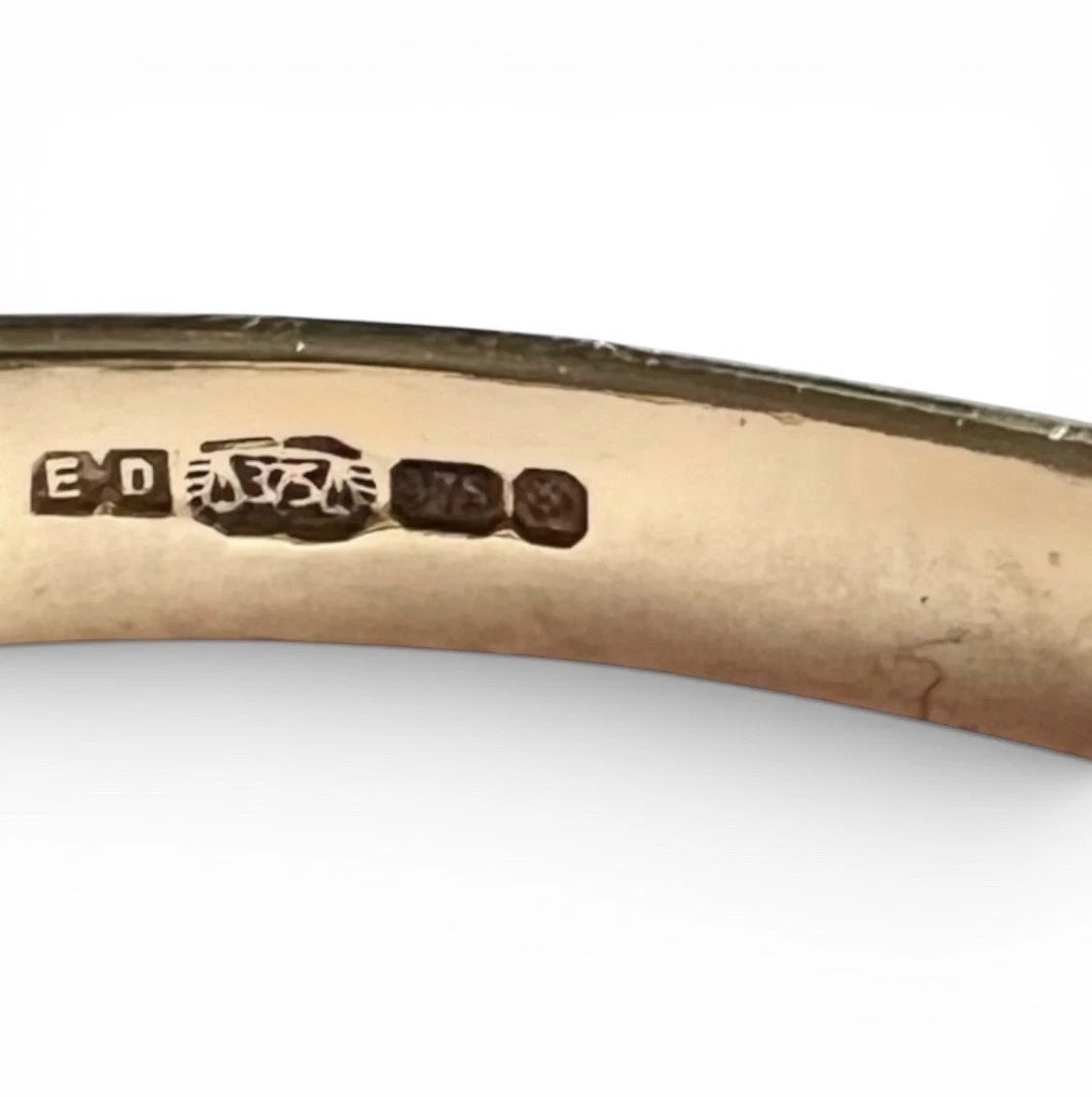 Close-up of a gold ring with engraved hallmark on a white background