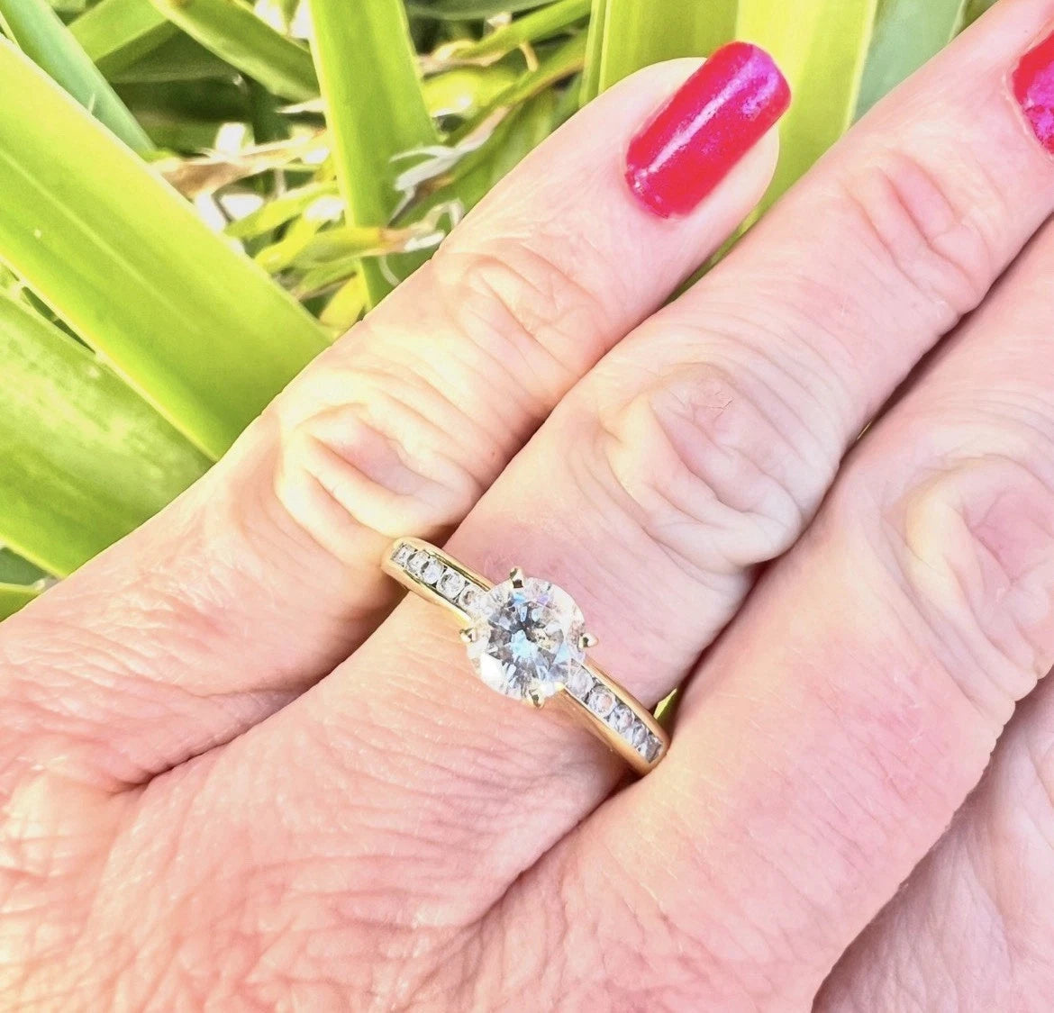Close-up of a hand wearing a gold ring with a CZ on a natural background
