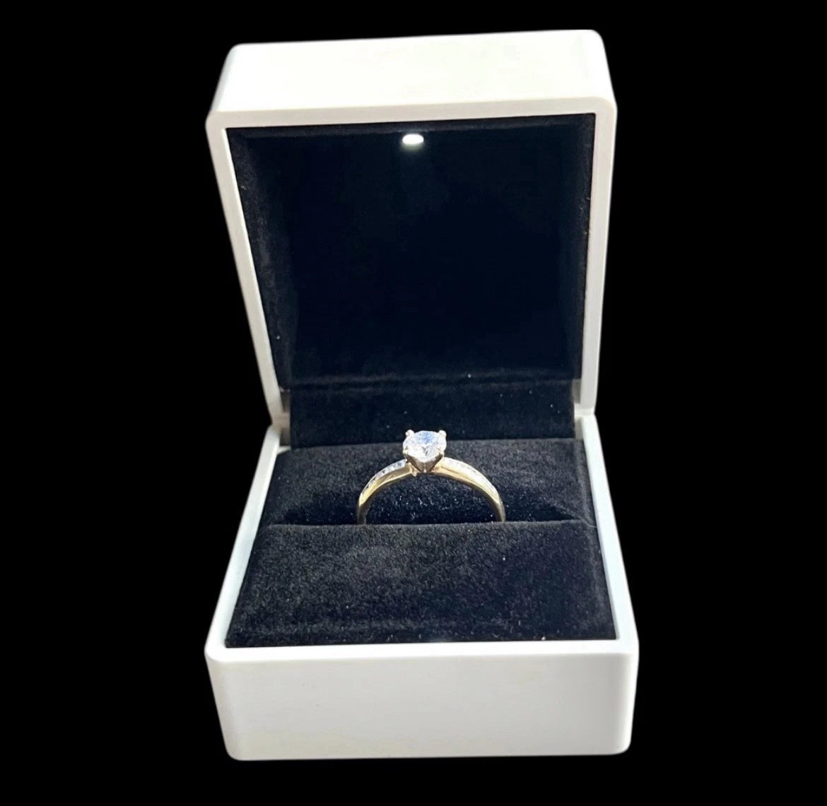 Gold solitaire ring with a CZ in an open jewellery box on a black background