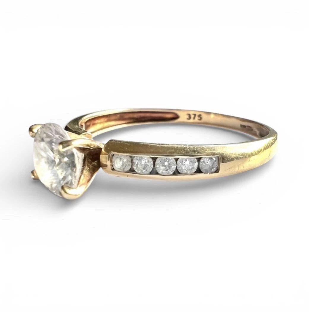 Gold ring with a large CZ and smaller diamonds on a white background. Close up side view 