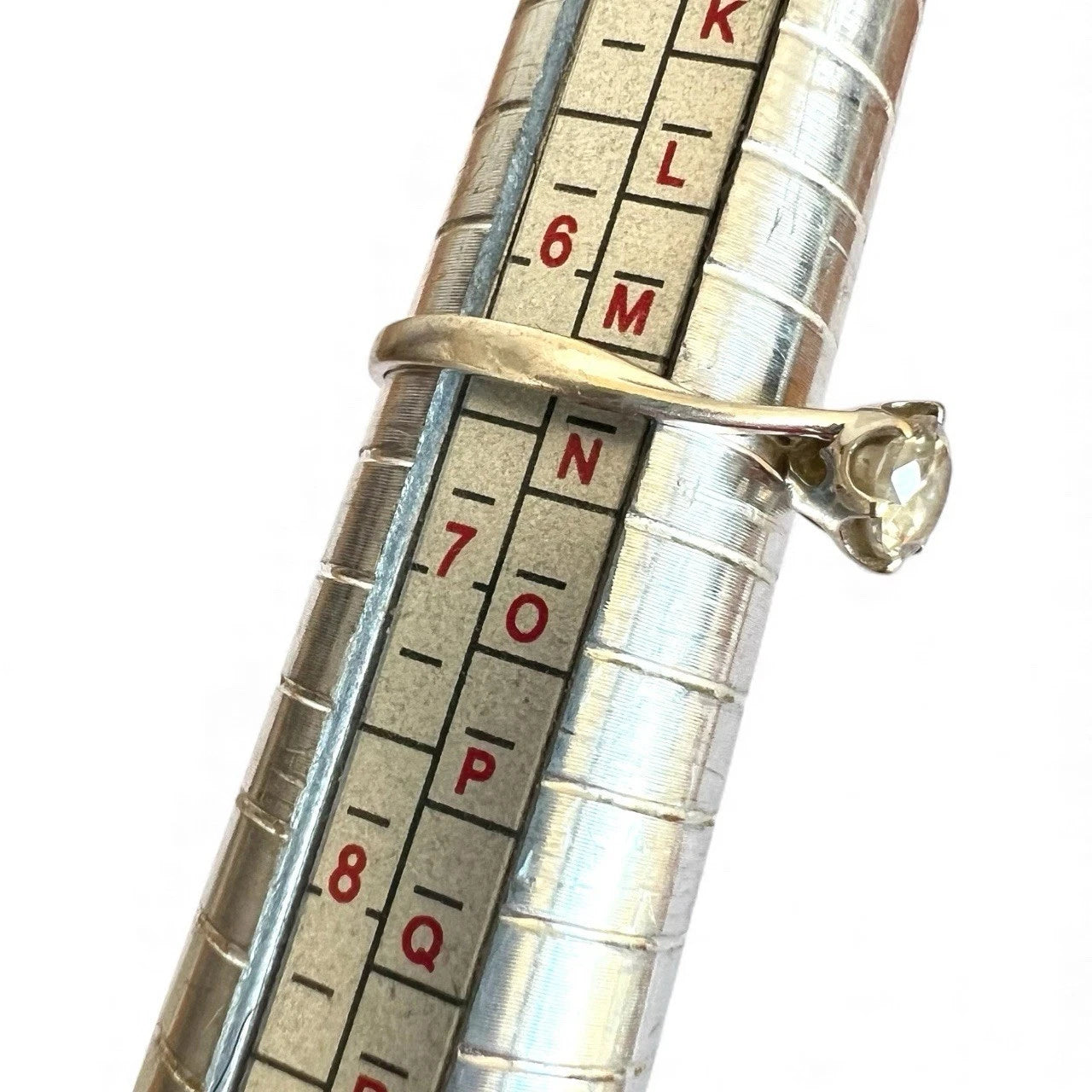Close-up of a silver measuring tool with a white gold ring on white background
