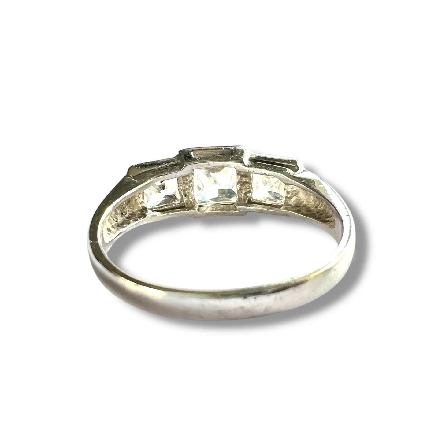 White gold ring with three cubic zirconia on a white background close up rear view of setting and gold band 