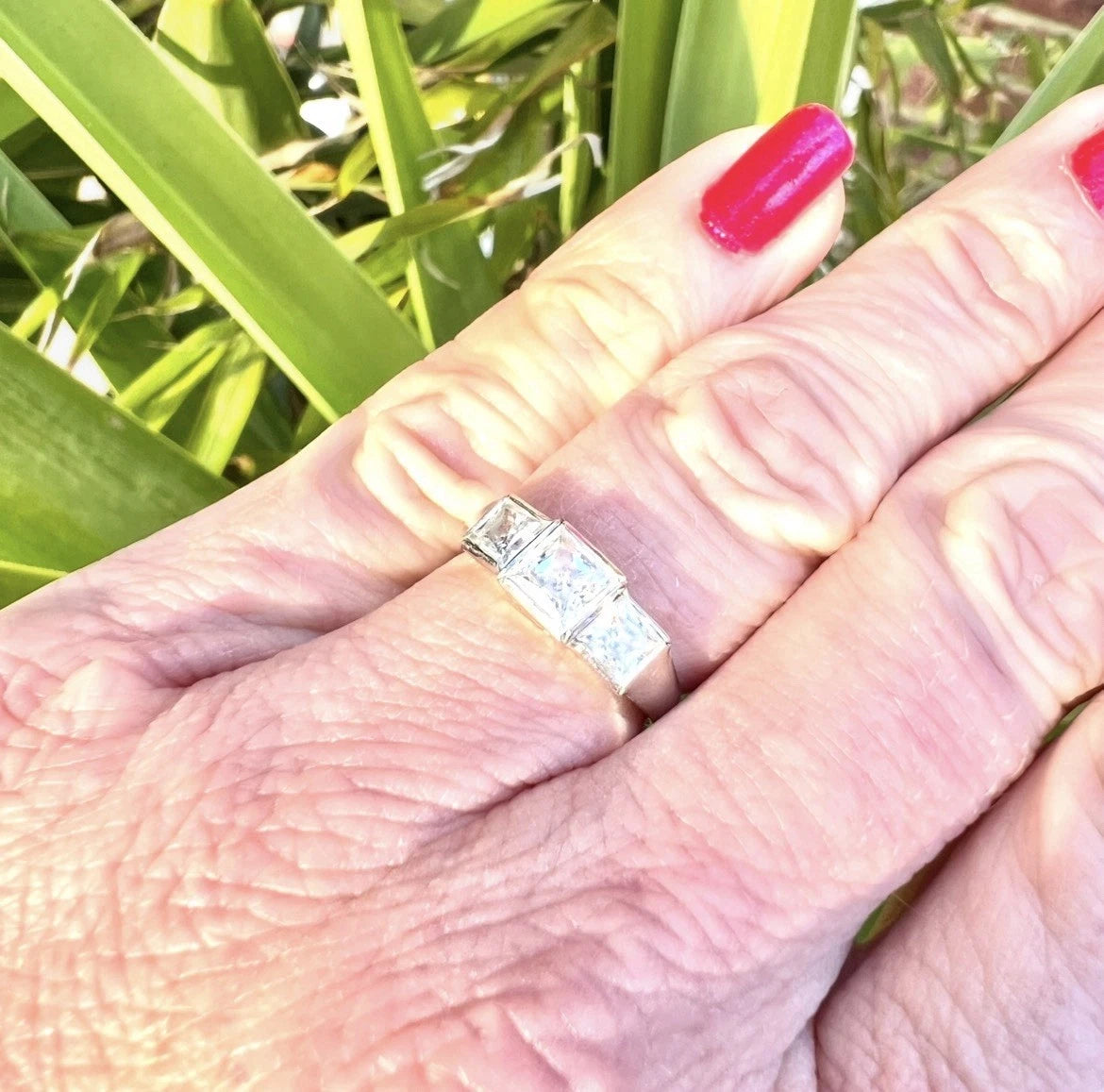Close-up of a hand wearing a cubic zirconia ring with a green leafy background