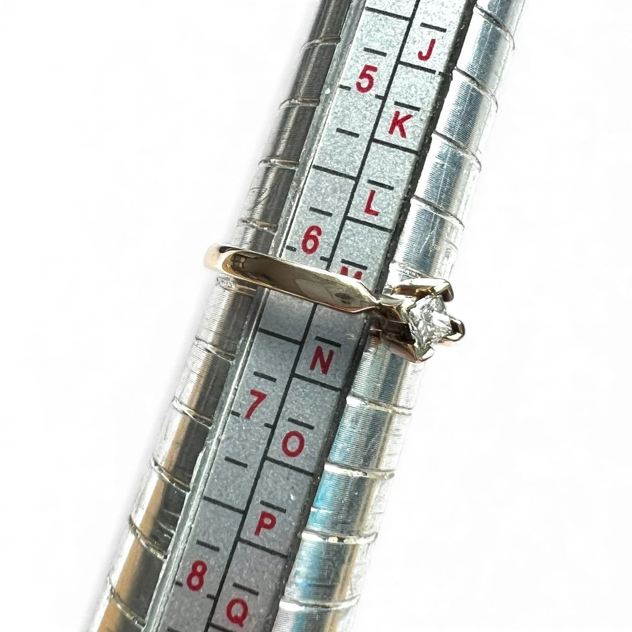 Gold ring with a diamond on a metal ring sizer for size measurement.