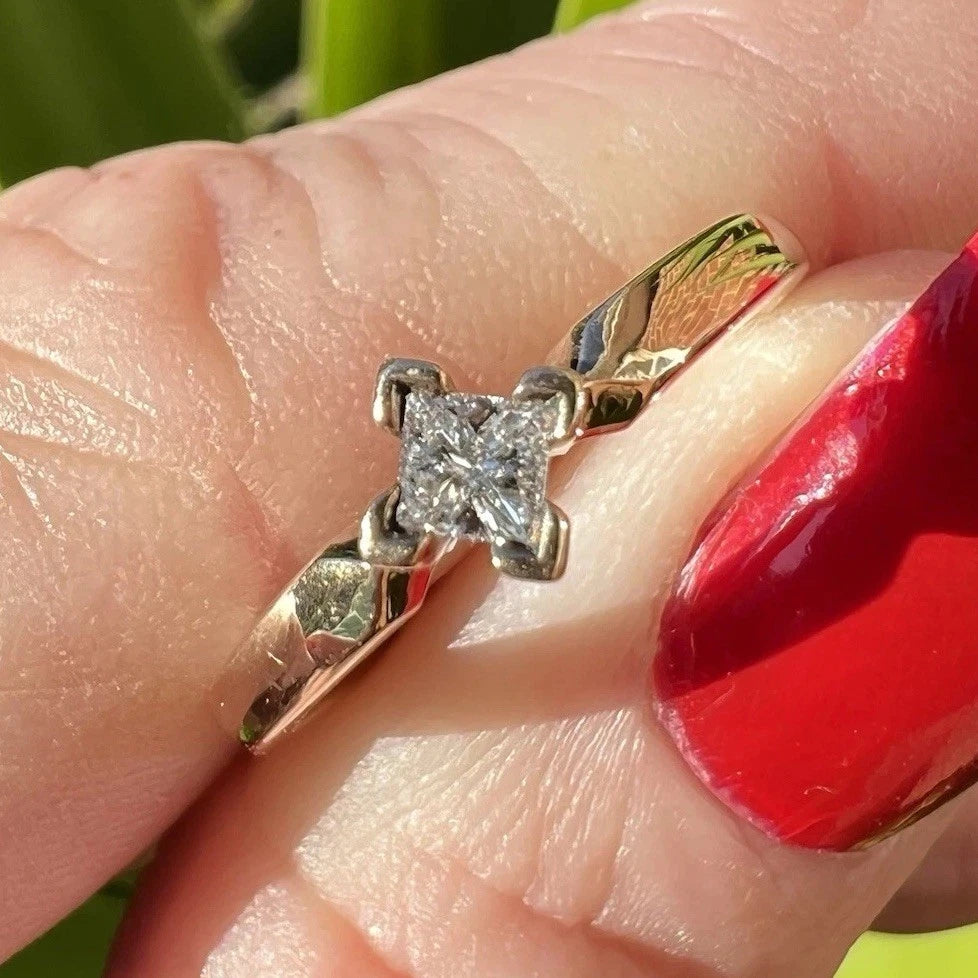 Gold ring with a diamond being held by a finger with red nail polish