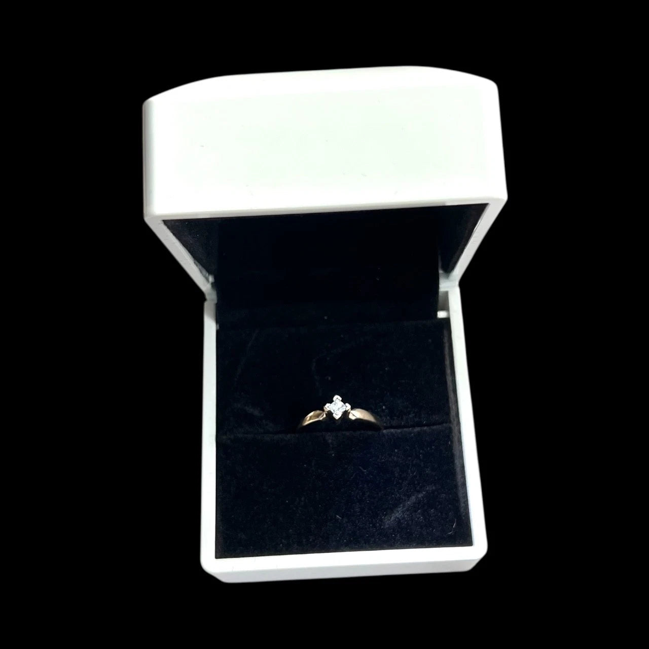 Diamond solitaire ring in a white box on a black background