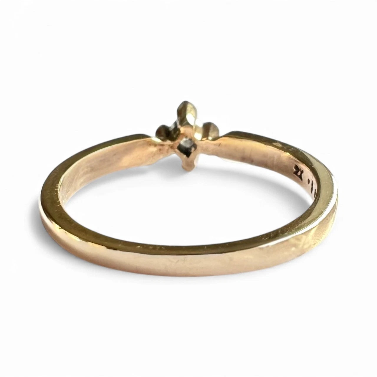 Gold ring with a small diamond on a white background. Close up rear view of setting and fold band. 