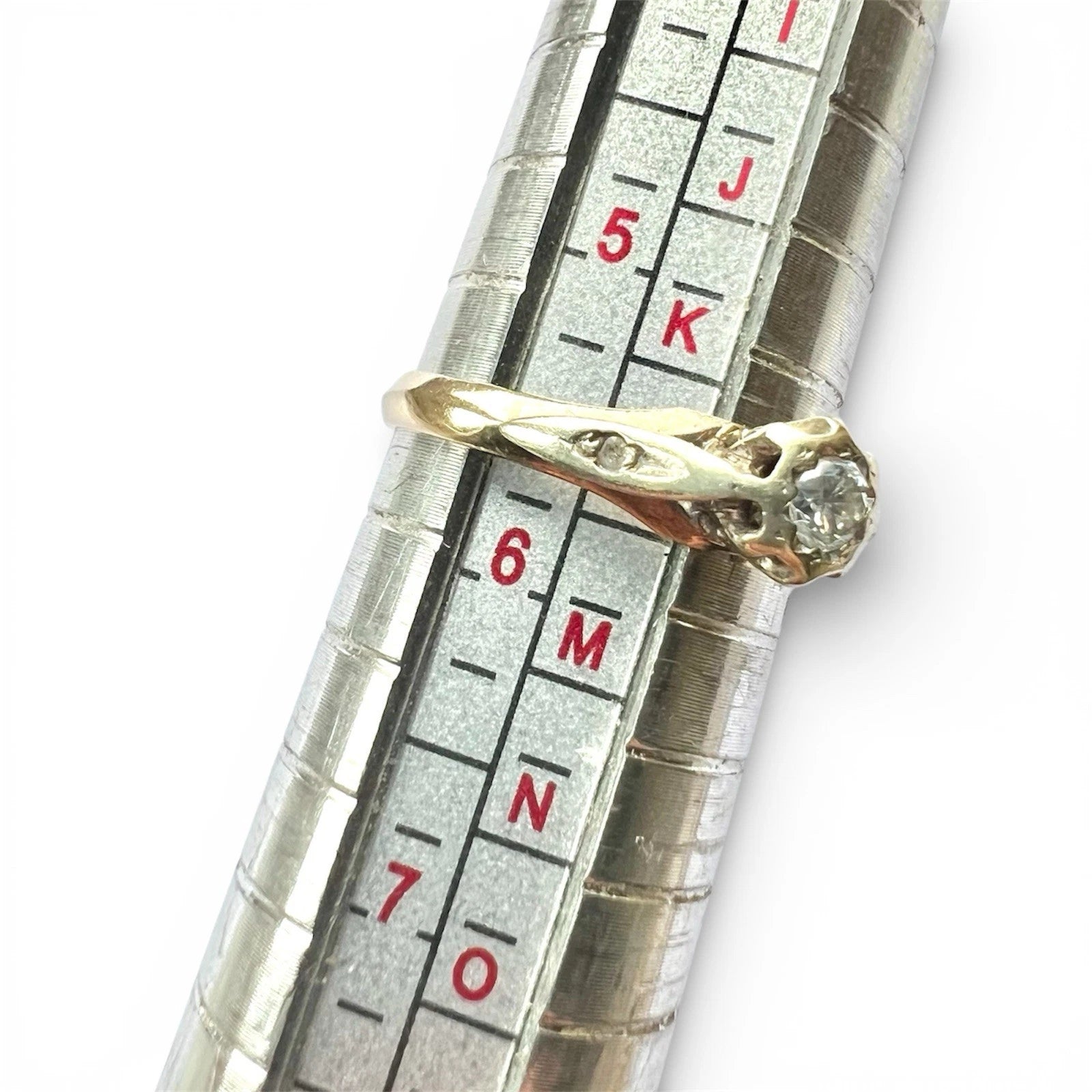 Gold ring being measured on a ruler with a white background