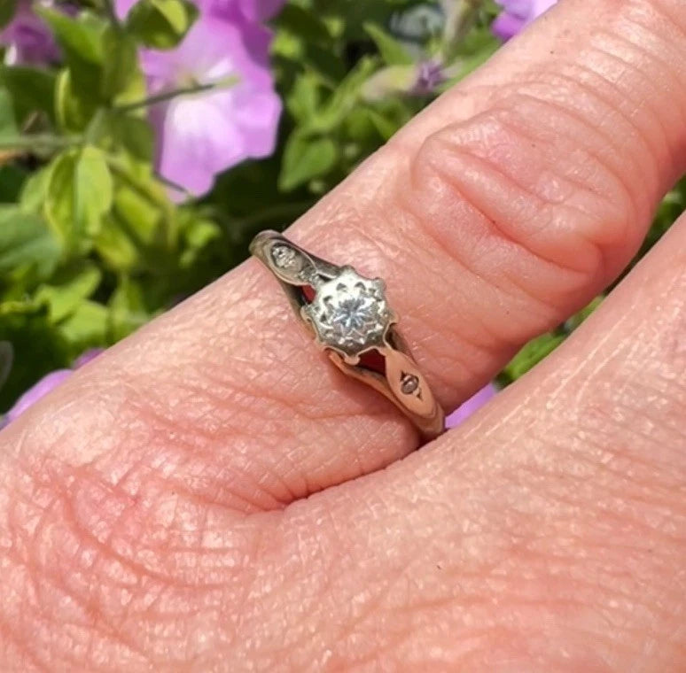 Gold ring with a diamond on a finger against a blurred floral background