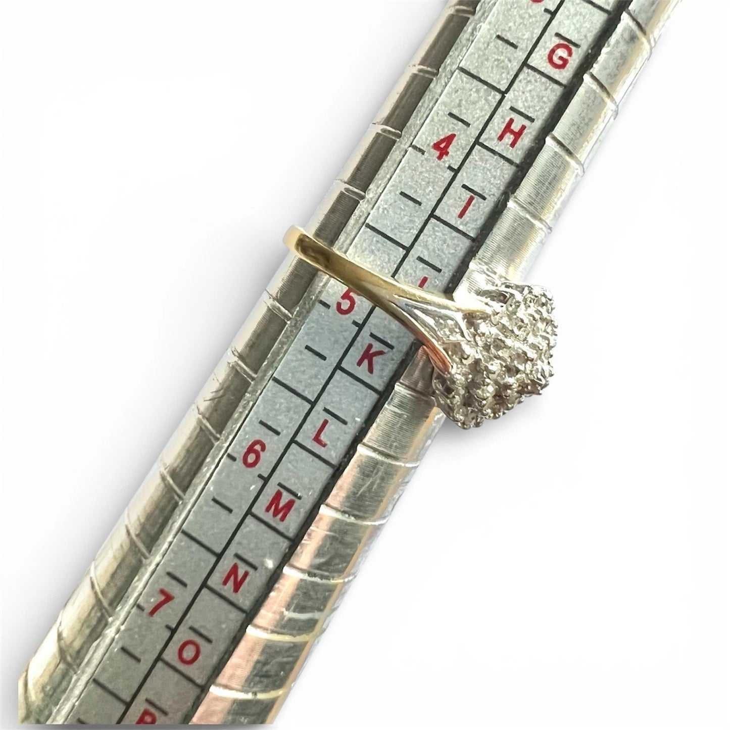 Gold diamond cluster rings on a ruler for size measurement against a white background