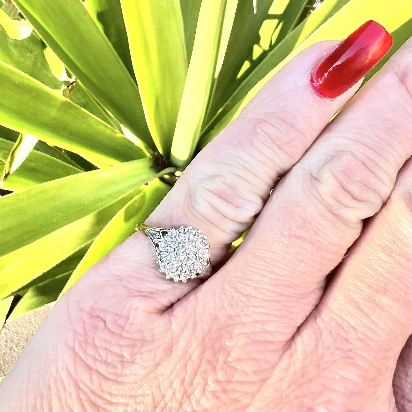 Hand wearing a diamond ring with green leaves in the background