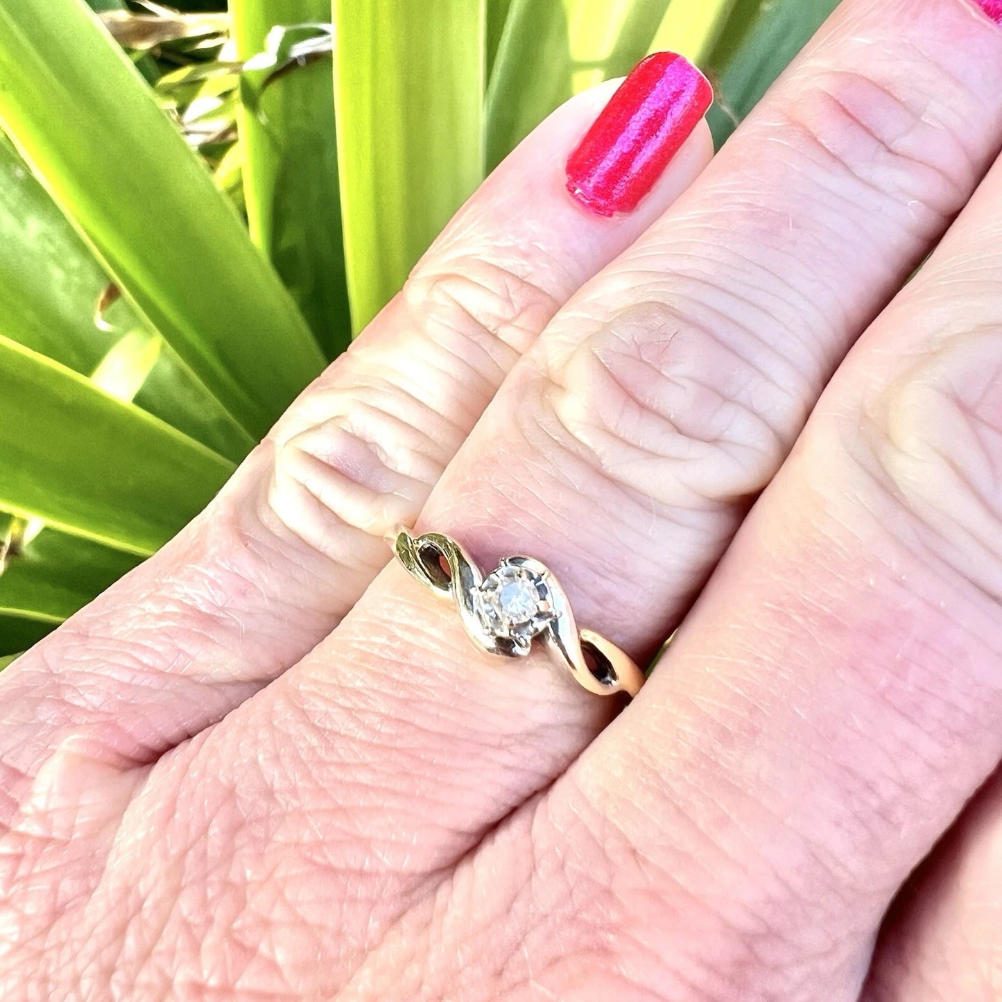 Gold ring with a diamond on a person's finger against a green plant background
