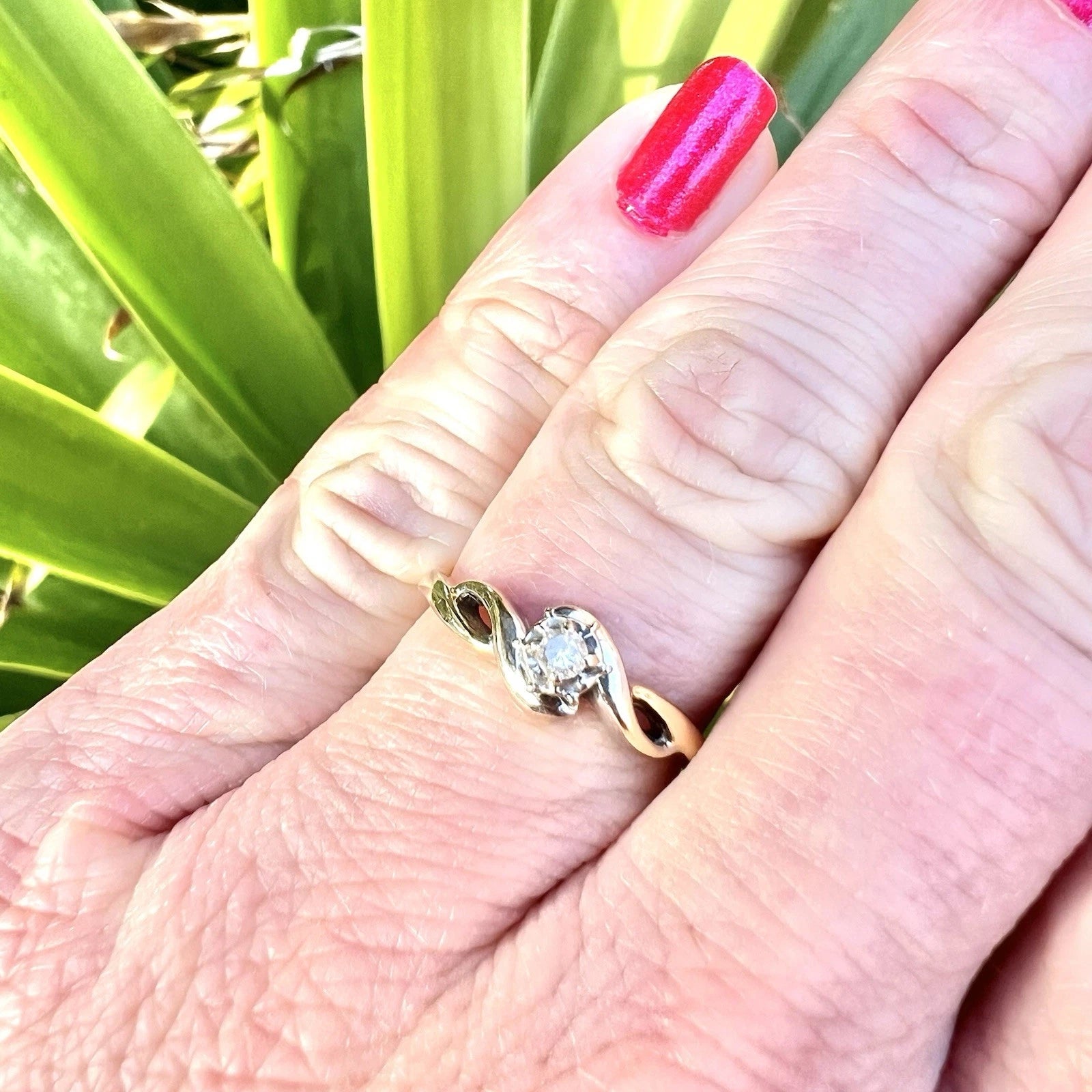 Gold ring with a diamond on a person's finger against a green plant background