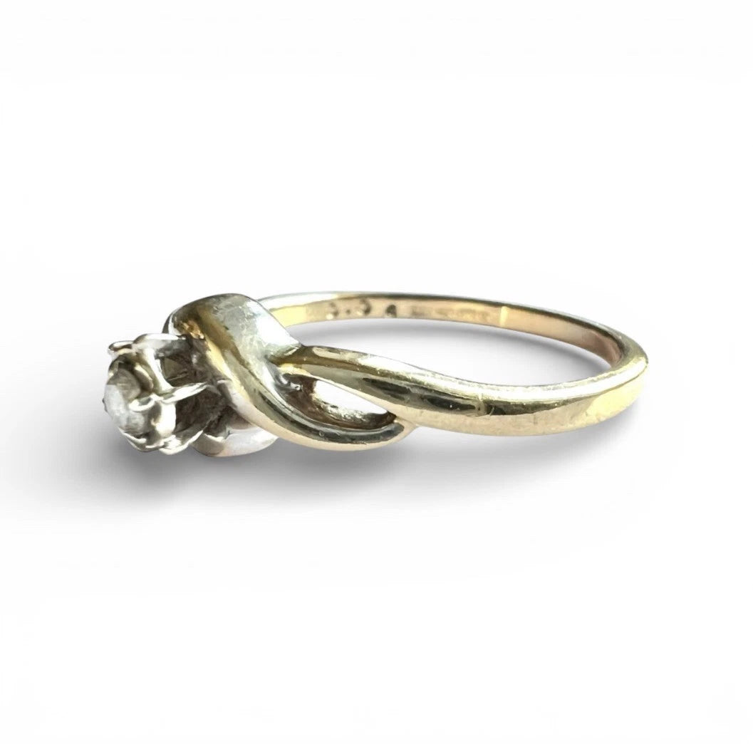 Gold ring with a diamond on a white background, close up side view of setting. 