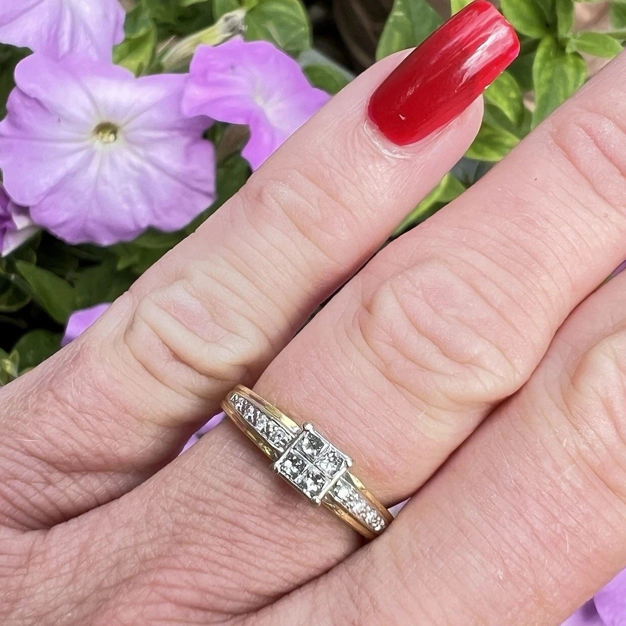 Gold ring with diamonds on a finger against a floral background