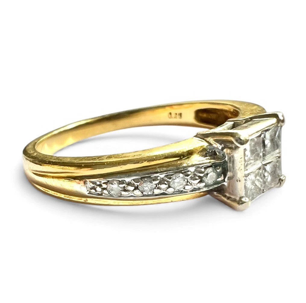 Gold ring with princess cut diamond and smaller diamonds on the band against a white background close up side view 